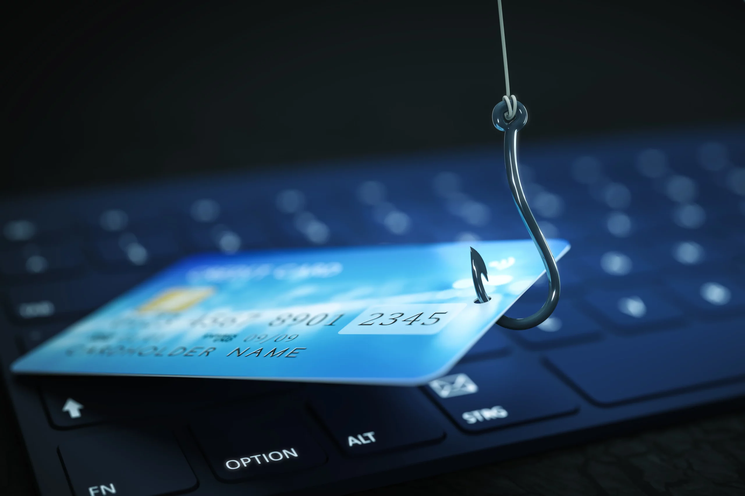 Phishing-and-Smishing A credit card on a fish hook sitting above a computer's keyboard.